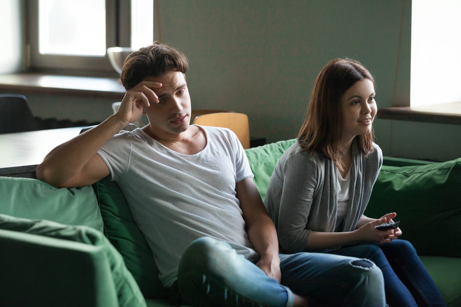 Unhappy disinterested boyfriend getting bored while excited lazy girlfriend spending time watching favorite reality show or soap opera tv series sitting on couch in living room holding remote control